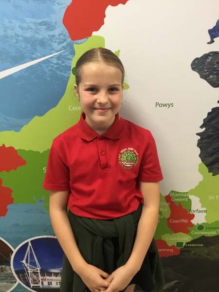 A girl smiling and wearing a polo shirt and standing infront of a map of Wales