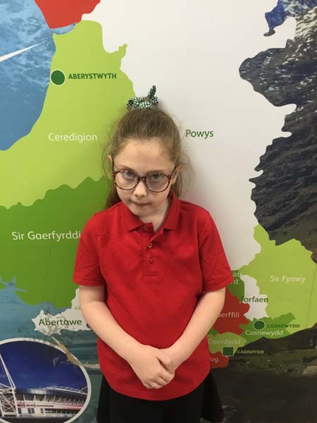 A girl wearing a red polo shirt and stands infront of a map of Wales
