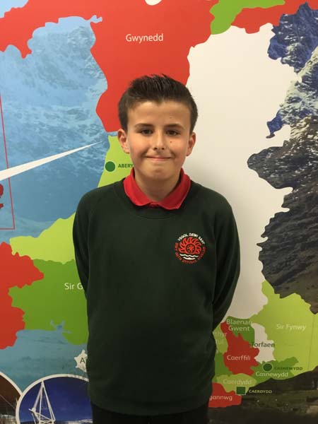 A boy wearing the school uniform while standing infront of a map of Wales